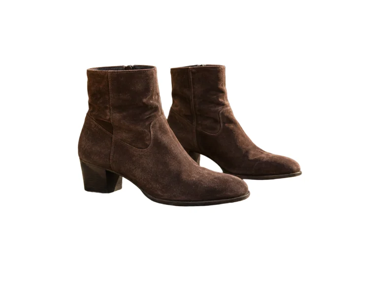 Brown suede boots resting on a stone bench — White background